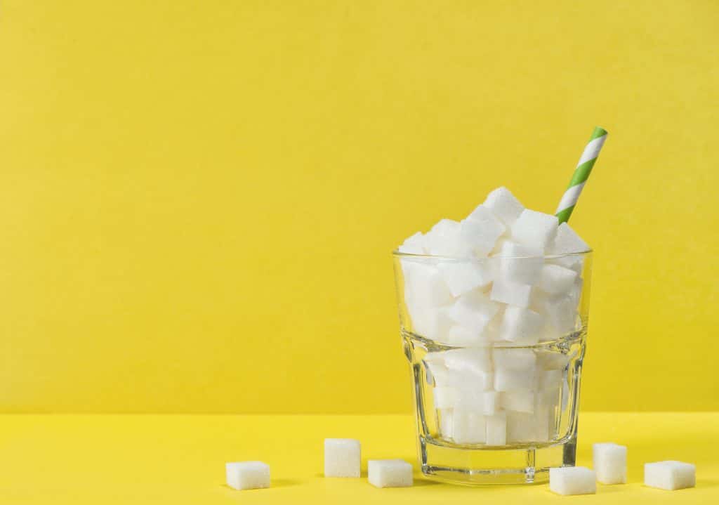 Un bicchiere di zollette di zucchero su sfondo giallo, simbolo di dolcezza e piacere.