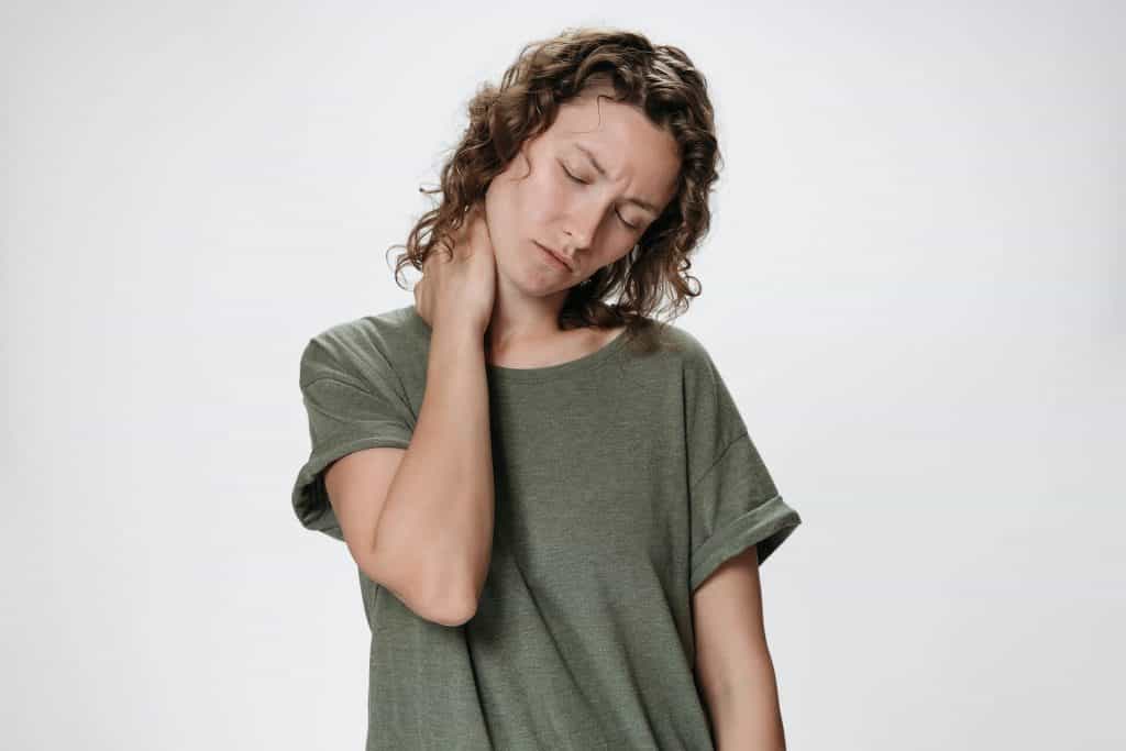 Eine Frau, die ein grünes T-Shirt trägt und die Hand am Hals hat, behandelt sich in Hamburg mit Osteopathie.
