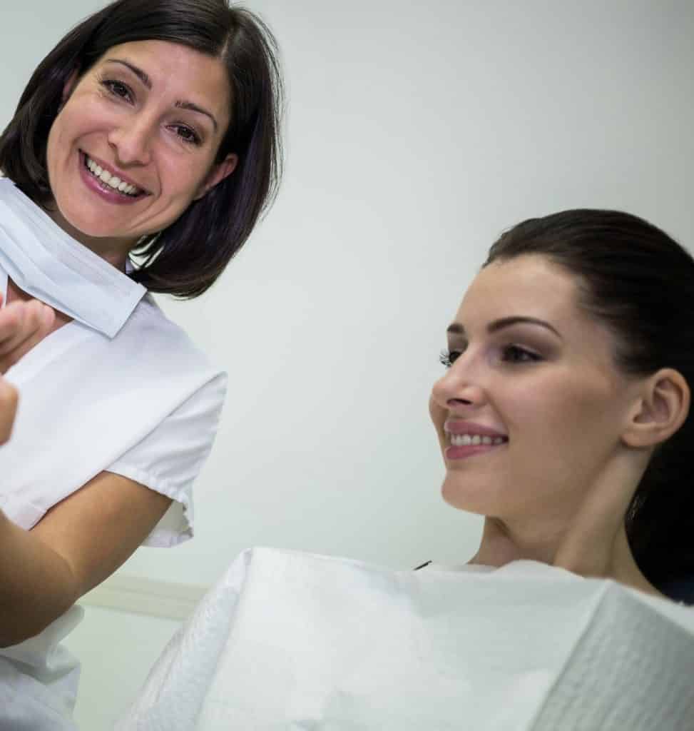 Eine Frau lächelt, während ein Zahnarzt ihre Zähne untersucht.