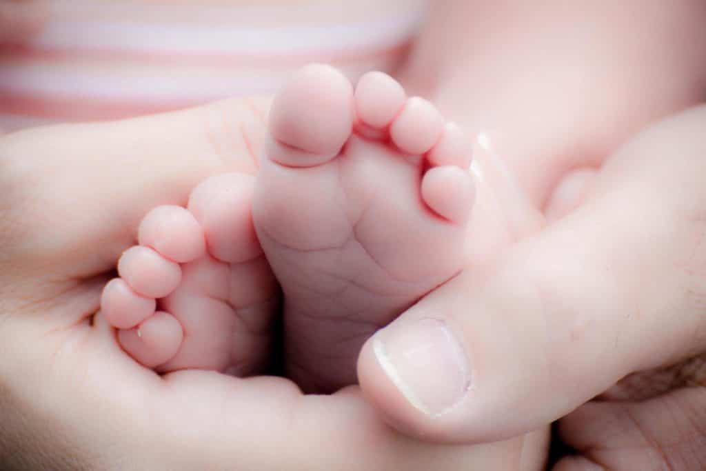 Eine Nahaufnahme der Füße eines Babys, die von einem Elternteil gehalten werden.