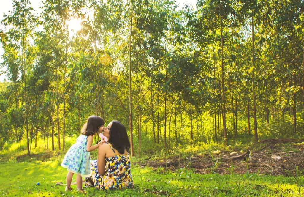 Eine Mutter und ihre Tochter genießen einen friedlichen Moment im Gras in einem ruhigen Wald.