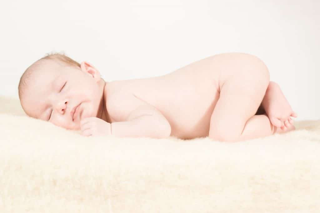 Ein neugeborenes Baby schläft friedlich auf einer weichen weißen Decke.