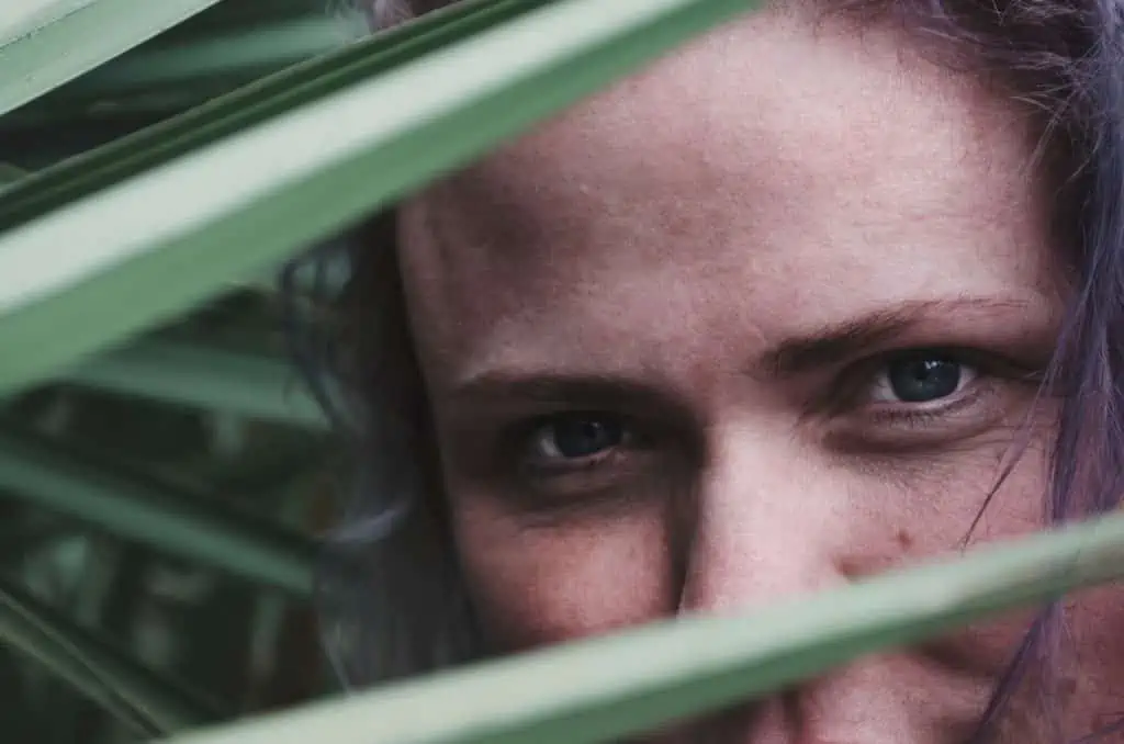 Eine Frau mit lila Haaren, die aus einer Pflanze hervorlugt, behandelt sich in Hamburg mit Sportosteopathie.