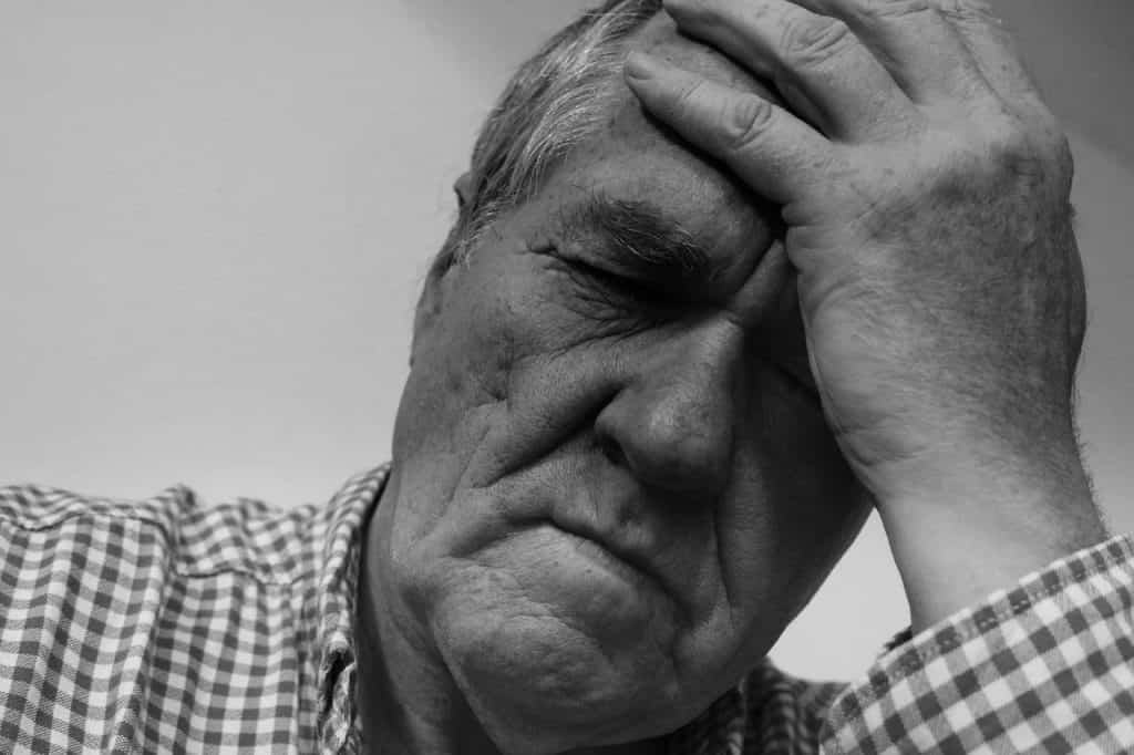 Ein Schwarz-Weiß-Foto eines älteren Mannes, der sich den Kopf hält und möglicherweise eine osteopathische Behandlung benötigt.