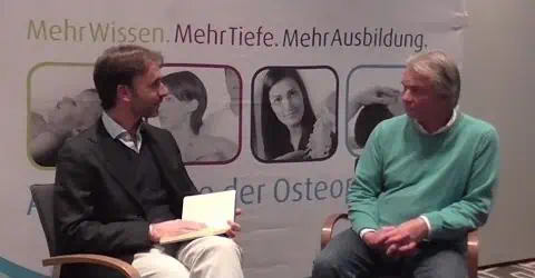 Zwei Männer sitzen auf Stühlen und reden miteinander, während sie eine Osteopathiebehandlung in Hamburg suchen.