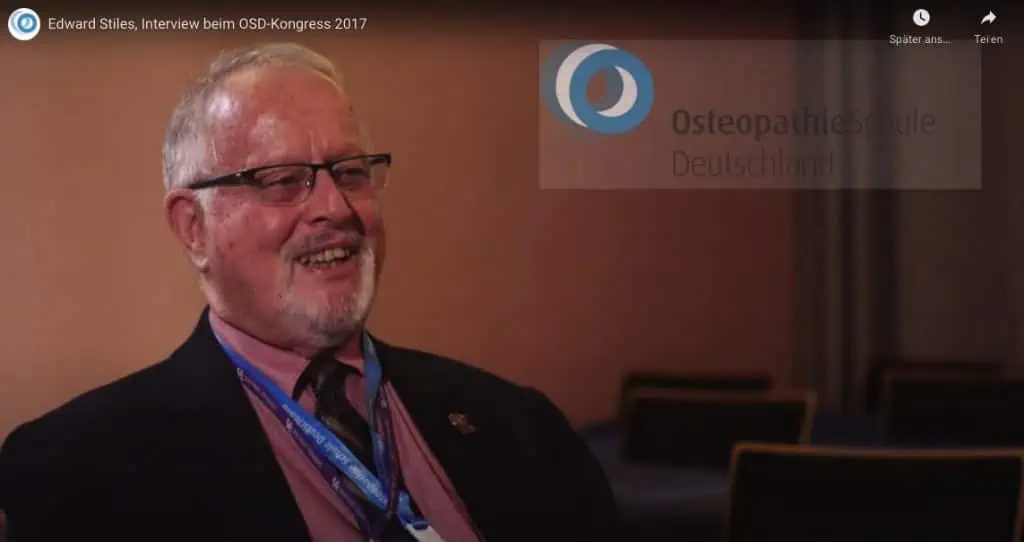 Ein Mann in Anzug und Krawatte lächelt für ein Sportosteopathie-Fotoshooting.