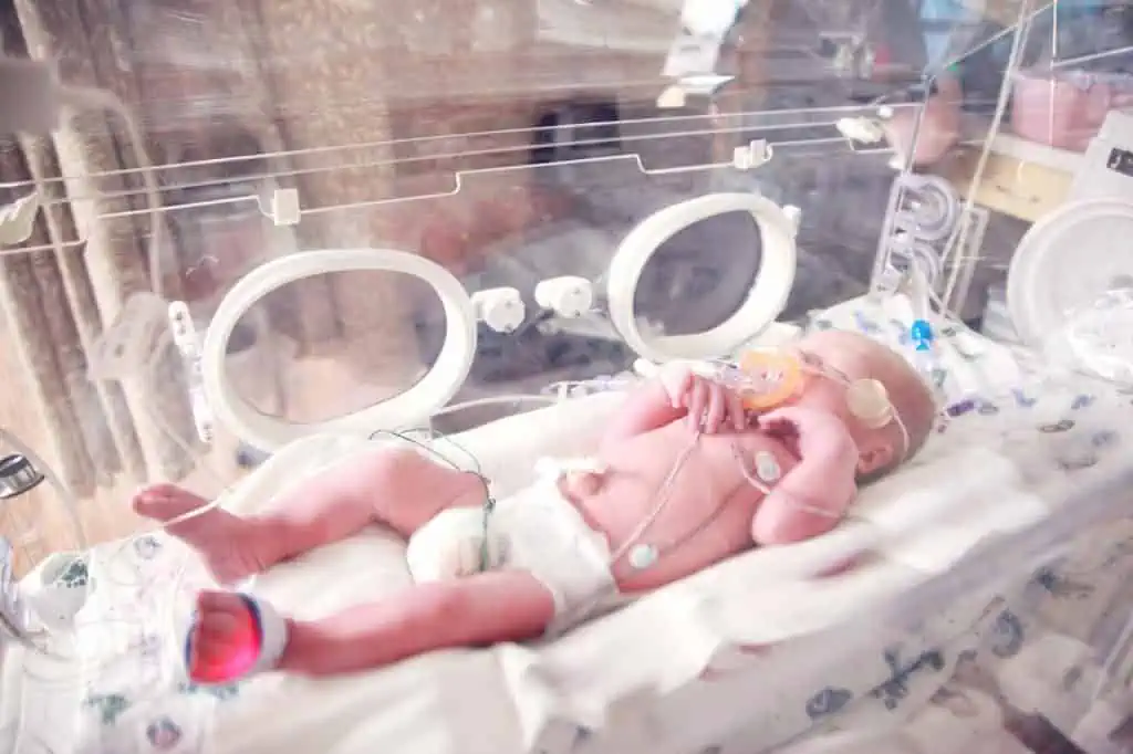 Ein Baby liegt mit einem Schnuller in einem Brutkasten und wird von einem erfahrenen Osteopathen in Hamburg betreut.