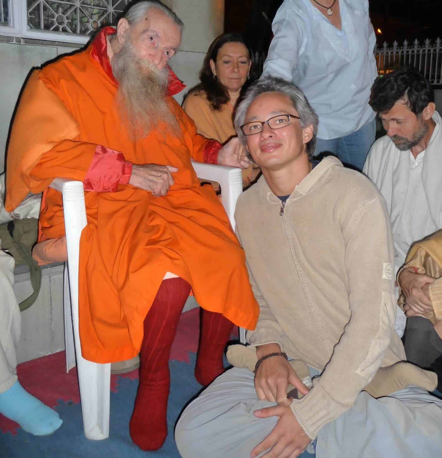 A group of people sit around a man in an orange robe during a paediatric osteopathy session.