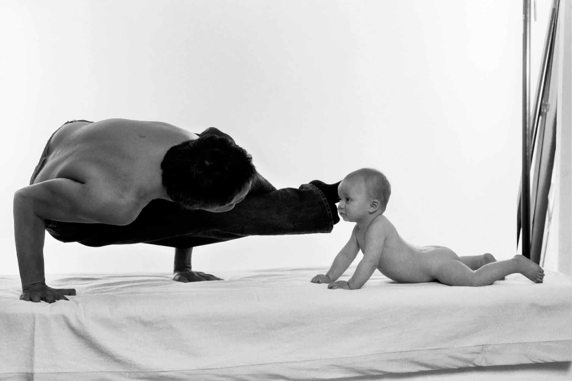 A man and a baby do yoga on a bed and look for the benefits of osteopathy in Hamburg.