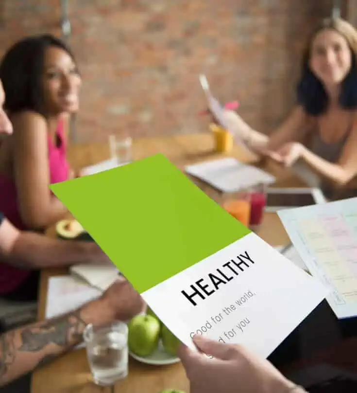 Eine Gruppe von Menschen sitzt an einem Tisch und hält ein grünes Papier mit dem Wort „gesund“.