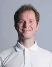 Ein Mann in einem weißen Poloshirt lächelt, während er Sportosteopathie praktiziert.