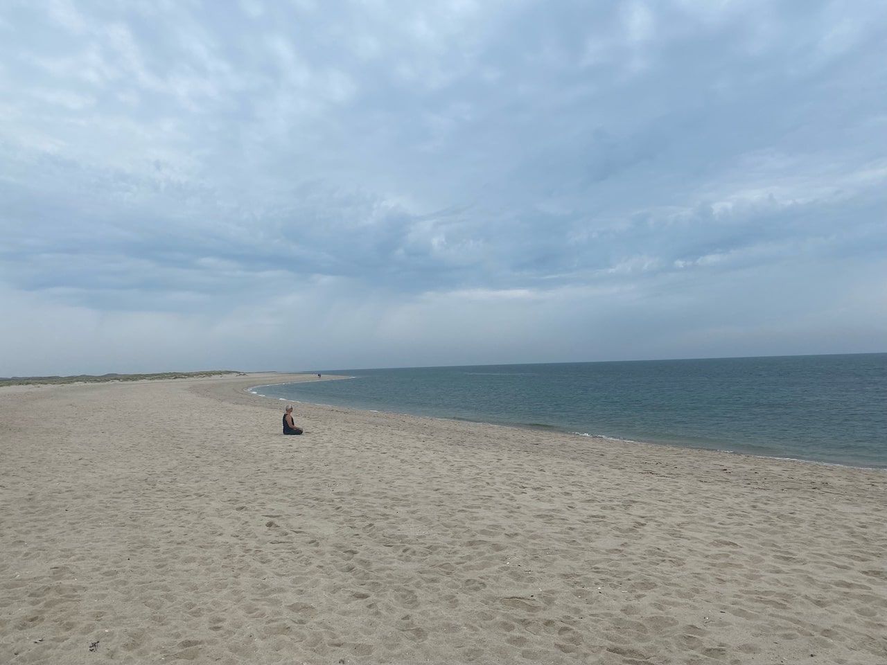 A person sits on a sandy beach under a cloudy sky and enjoys the peace and beauty of the natural landscape.