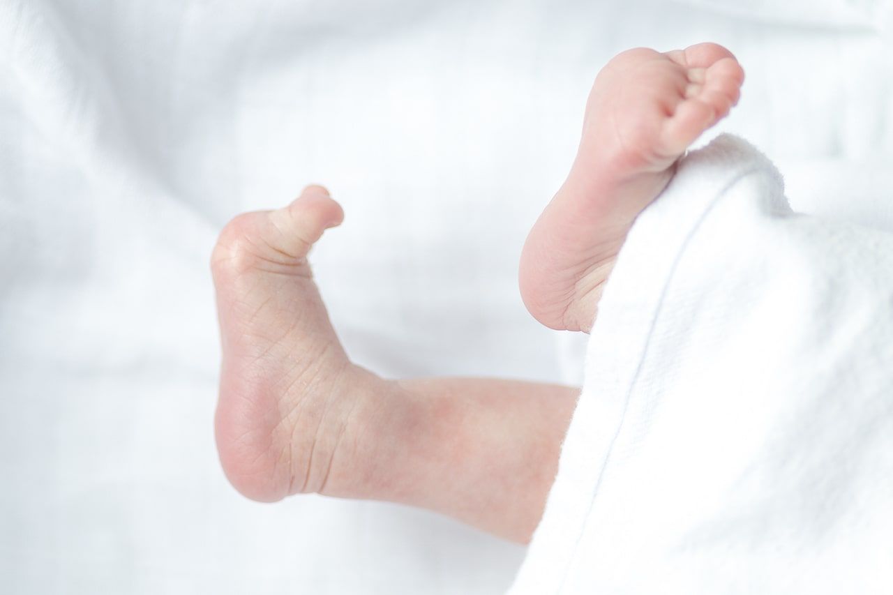 Eine Nahaufnahme der Füße eines Babys auf einer weißen Decke, die die sanfte Berührung und die Bedeutung der Kinderosteopathie hervorhebt.