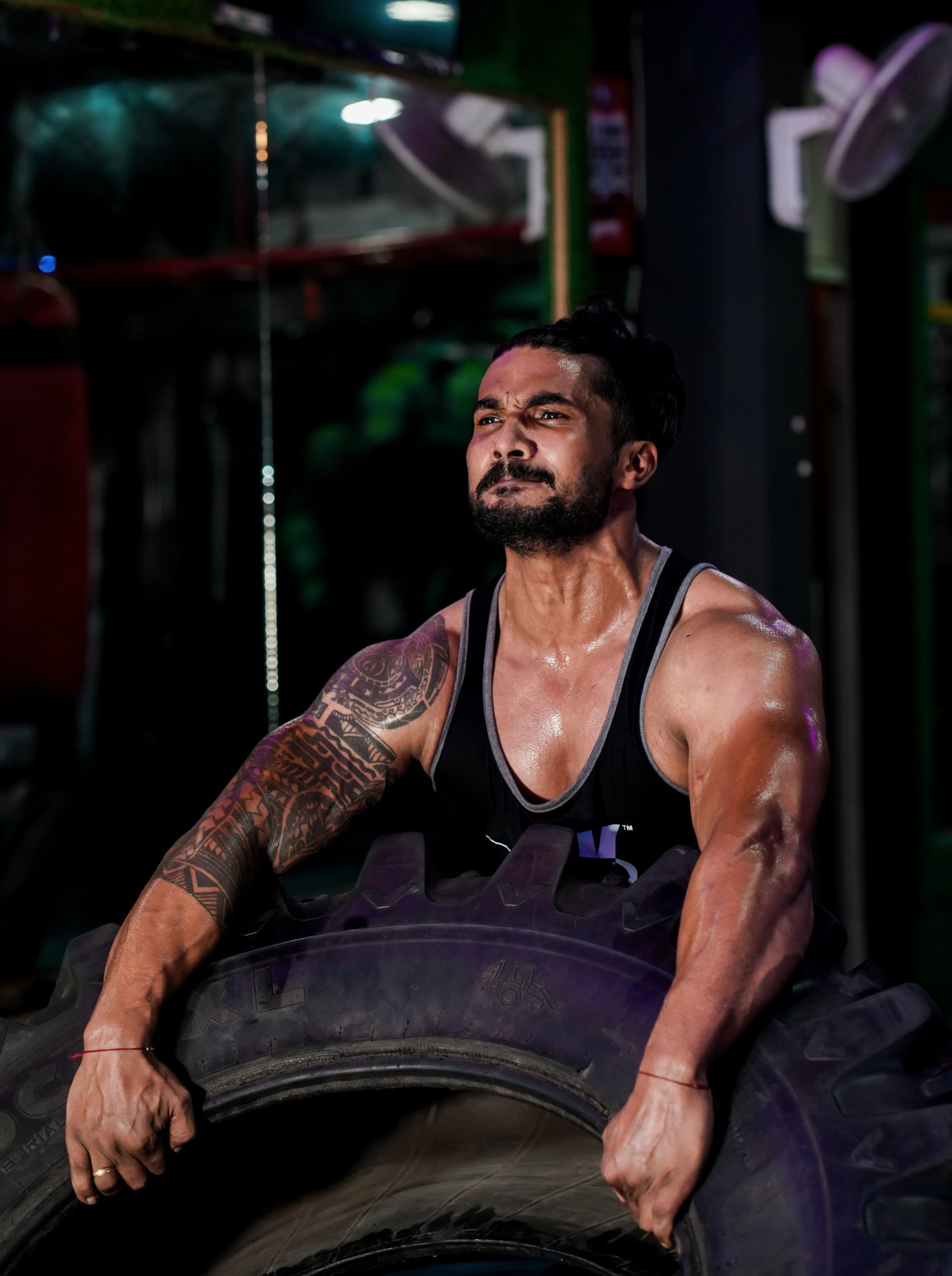 Un homme est assis sur un pneu dans une salle de sport et pratique l'ostéopathie sportive.