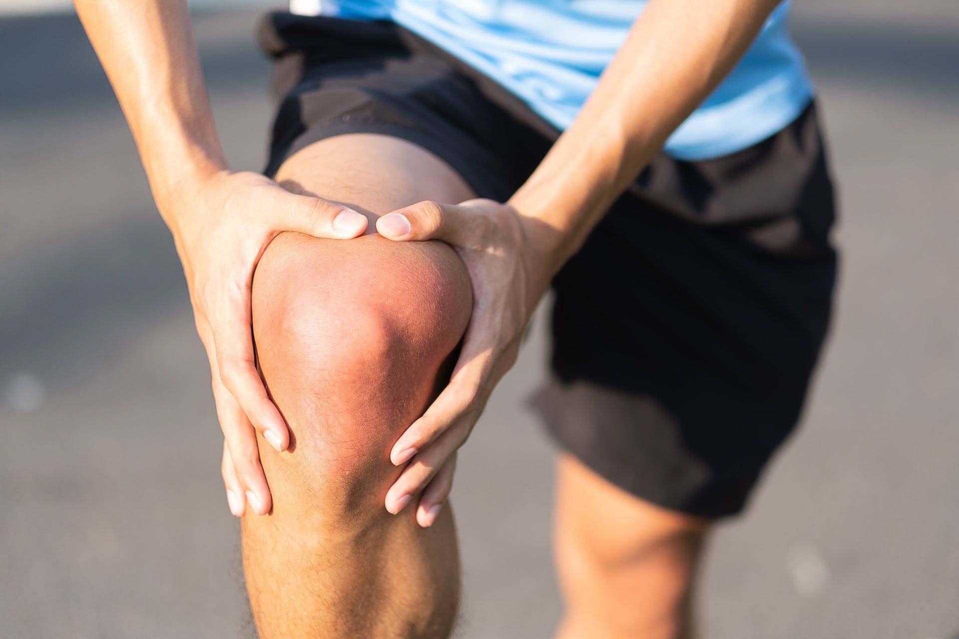 Ένας άνδρας με τραυματισμό στο γόνατο κρατάει το γόνατό του και αναζητά αθλητική οστεοπαθητική θεραπεία.