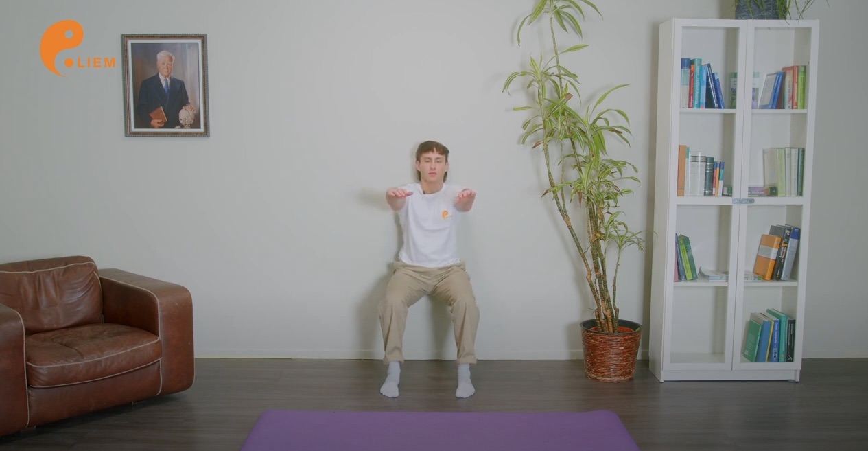 Ein Mann führt unter Einbeziehung einer Armbewegung eine Yoga-Übung in einem Wohnzimmer durch.