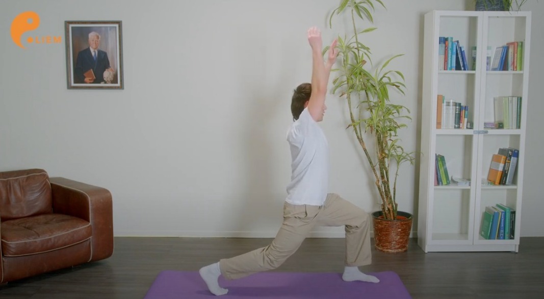Mann führt in einer ruhigen Innenumgebung eine Yoga-Pose mit dem Großen Armkreis aus.