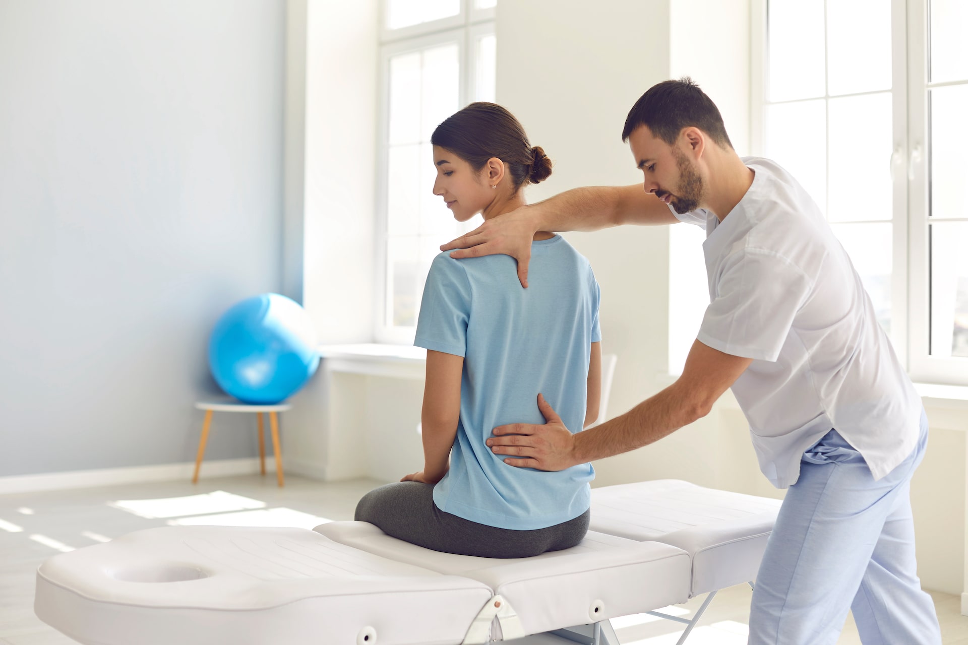 In einem gut beleuchteten Rehabilitationsraum unterstützt eine Physiotherapeutin eine junge Frau bei ihren Übungen gegen Rückenschmerzen.